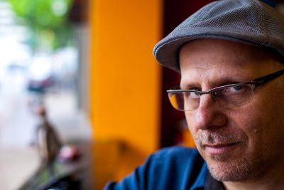 Eric Weiner sits with a cap on and glasses in an outdoor cafe.
